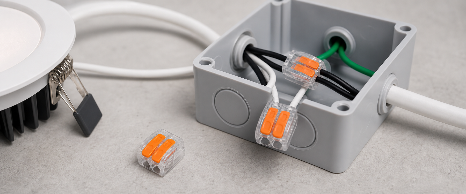 Lever wire connectors inside a gray electrical junction box connecting white and black wires, with two loose orange lever connectors placed beside the box on a work surface.