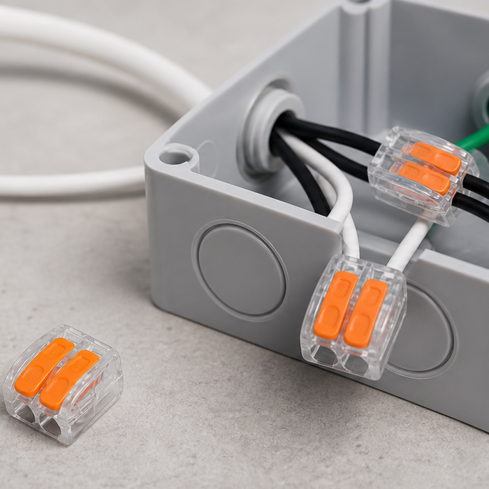 Lever wire connectors inside a gray electrical junction box connecting white and black wires, with two loose orange lever connectors placed beside the box on a work surface.