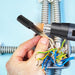 Hand using a tool to work on electrical wiring against a light blue background